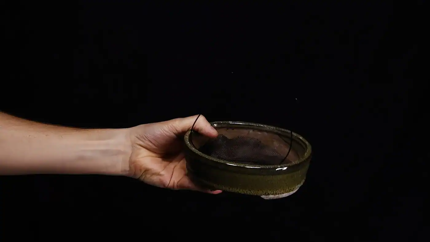 A bonsai pot prepped with mesh over the drainage holes and anchoring wire threaded through